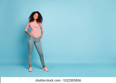 Full length photo of amazing pretty dark skin lady with adorable smile holding hands in pockets wear casual clothes isolated pastel blue color background