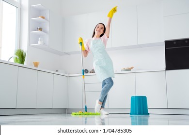Full length photo of asian ethnicity housewife general cleaning disinfecting all surfaces infection safety hold mop clean floor wear gloves apron t-shirt jeans stand kitchen indoors