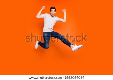Full length photo of attractive crazy guy jump high supporting favorite football team match game goal wear striped t-shirt jeans shoes isolated bright orange color background