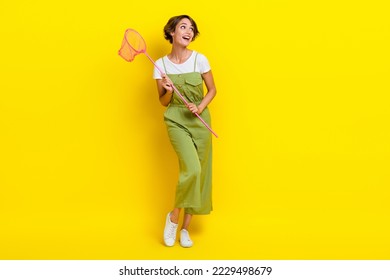 Fotografía de longitud completa de la atractiva joven de pelo castaño bob sujetando un palo de red luce espacio vacío soñando con lo aislado en el fondo de color amarillo