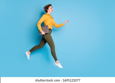Full length photo of beautiful pretty business lady jump high hold notebook rushing conference wear yellow shirt green pants shoes isolated bright blue color background