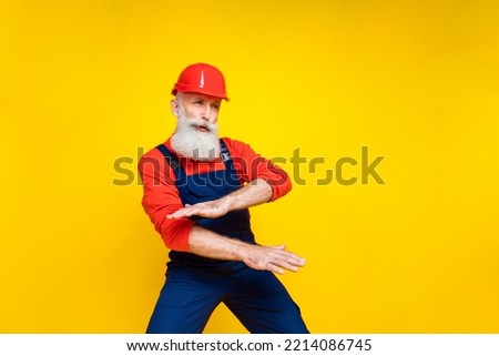 Full length photo of carefree senior engineer with white beard red helmet dancing look empty space isolated on yellow color background