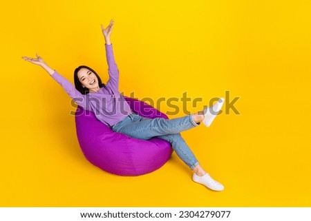 Full length photo of careless girl chilling hands up relax time dormitory beanbag vacation weekend isolated on yellow color background