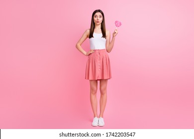 Full Length Photo Of Charming Funny Lady Send Air Kisses Hold Big Heart Shape Lollipop On Stick Good Mood Wear White Singlet Dotted Short Skirt Shoes Isolated Pastel Pink Color Background