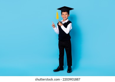 Full length photo of charming funny small boy wear black waistcoat graduation cap pointing empty space isolated blue color background - Powered by Shutterstock