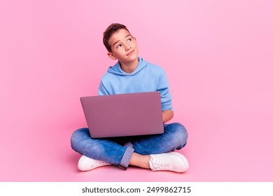 Full length photo of charming teen boy sit floor netbook look empty space dressed stylish blue garment isolated on pink color background - Powered by Shutterstock