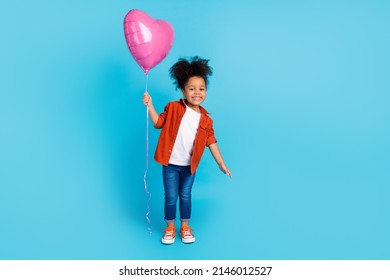 Full length photo of cheerful cute little lady receive birthday present hold heart shaped balloon isolated on blue color background