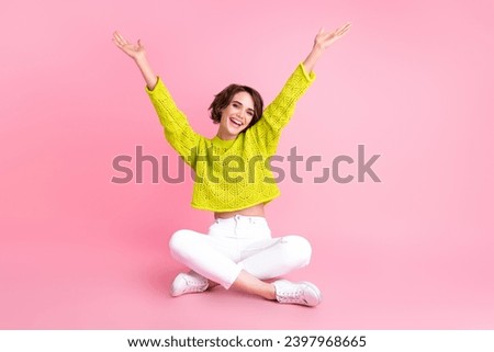 Full length photo of cheerful excited girl dressed neon sweater sitting legs crossed rising hands arms isolated pink color background