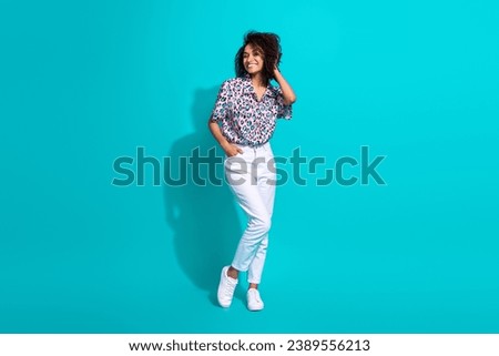 Full length photo of cheerful gorgeous girl dressed trendy clothes hand touch curly hairdo empty space isolated on cyan color background