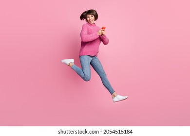 Full Length Photo Of Cheerful Happy Young Woman Jump Up Hold Hands Phone Smile Isolated On Pink Color Background