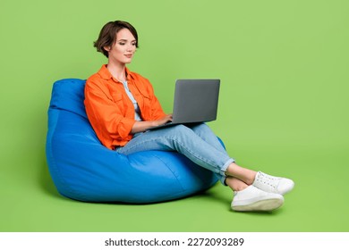 Full length photo of cheerful woman wear denim jacket bean bag typing emails gadget empty space isolated green color background - Powered by Shutterstock