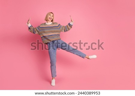 Full length photo of cheerful woman dressed print sweater denim pants dancing look at promo empty space isolated on pink color background
