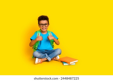 Full length photo of confident cheeful preteen boy wear blue t-shirt reading novel showing two thumbs up empty space isolated yellow color background