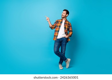 Full length photo of cool guy wear checkered shirt denim pants directing look at discount empty space isolated on blue color background - Powered by Shutterstock