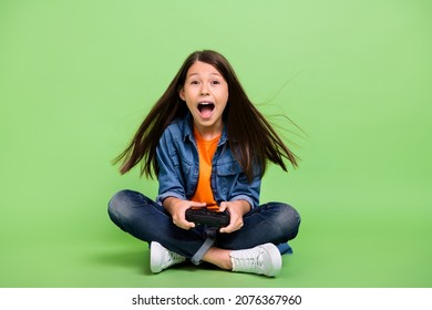 Full Length Photo Of Cool Small Girl Play Station Yell Wear Shirt Jeans Shoes Isolated On Green Background