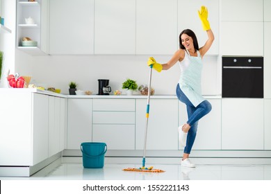 Full length photo of crazy cheerful gilr wash floor in kitchen with mop want have relax fun imagine she dances clubbing raising hands screaming wearing dotted apron indoors