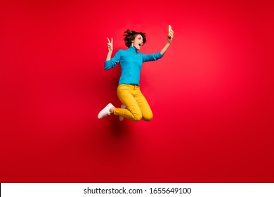 Full Length Photo Of Crazy Funky Bob Brunette Hair Girl Jump Enjoy Spring Fall Holiday Make Selfie V-sign Smartphone Blogging Wear Blue Sweater Yellow Outfit Isolated Bright Red Color Background