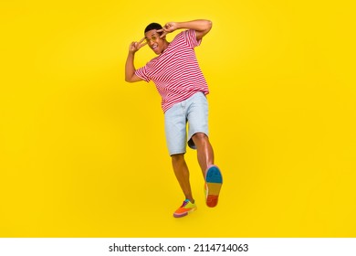 Full Length Photo Of Crazy Guy Dance Make V-sign Eye Wear Red Striped Shorts Sneakers Isolated Over Bright Yellow Color Background