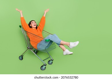 Full length photo of crazy lady ride push cart raise arms up amazed autumn bargain isolated over green color background