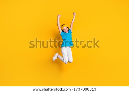 Full length photo of crazy little lady jump high up good mood celebrate competition winning raise fists wear casual blue t-shirt headband trousers shoes isolated yellow color background