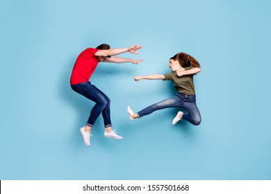 Full length photo of crazy mad two people spouses woman disagree jump fight kick man fall wear green red t-shirt denim jeans sneakers isolated over blue color background