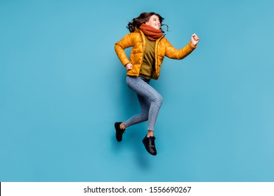 Full length photo of crazy millennial lady jumping high running speed shopping season discounts wear stylish windbreaker jeans scarf pullover isolated blue color background - Shutterstock ID 1556690267