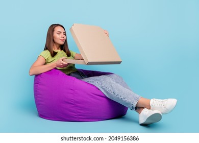 Full length photo of cute brunette millennial lady sit on bag eat pizza wear t-shirt jeans sneakers isolated on blue color background