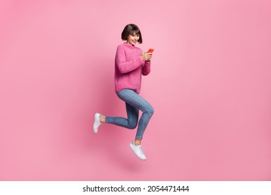 Full length photo of cute charming happy woman jump up hold hands phone smile isolated on pink color background