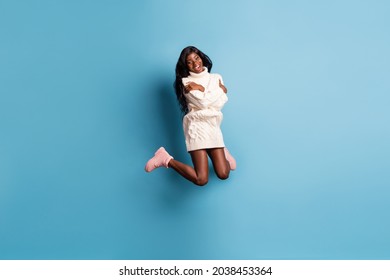 Full Length Photo Of Cute Dark Skin Woman Dressed White Winter Clothes Jumping Hugging Herself Isolated Blue Color Background