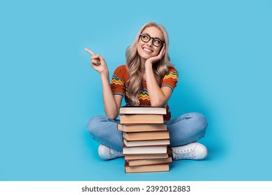 Full length photo of cute dreamy lady wear print shirt spectacles reading book stack pile showing empty space isolated blue color background - Powered by Shutterstock