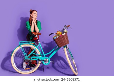 Full length photo of cute girl wear shirt print trousers lean on bicycle look at promo empty space isolated on violet color background - Powered by Shutterstock