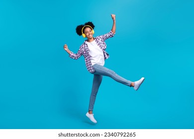 Full length photo of cute sweet girl dressed checkered shirt jumping walking enjoying music isolated blue color background - Powered by Shutterstock