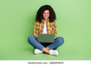 Full Length Photo Of Cute Volume Hairstyle Young Lady Sit Type Laptop Wear Spectacles Yellow Shirt Jeans Shoes Isolated On Green Background