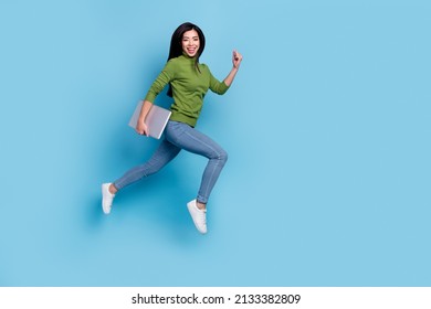 Full Length Photo Of Cute Young Brunette Lady Run With Laptop Wear Jumper Jeans Sneakers Isolated On Blue Background.