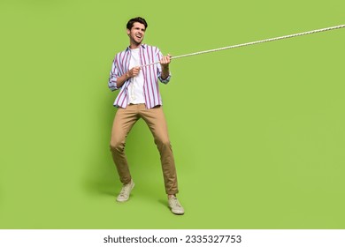 Full length photo of determined man with stubble dressed striped shirt pull rope from empty space isolated on green color background - Powered by Shutterstock