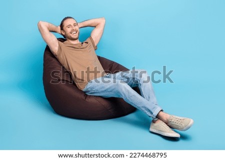Full length photo of dreamy cheerful man wear beige t-shirt bean bag arms behind head emtpy space isolated blue color background