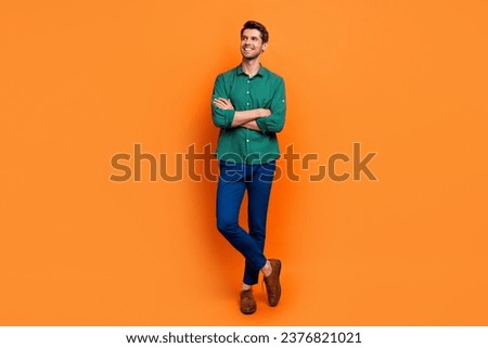 Full length photo of dreamy confident guy wear green shirt arms crossed looking empty space isolated orange color background