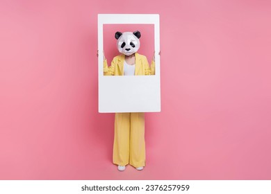 Full length photo of eccentric 3d panda mask person hands hold paper album set card isolated on pink color background