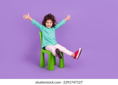 Full length photo of excited funky small kid wear turquoise shirt sitting chair rising hands arms empty space isolated violet color background - Powered by Shutterstock