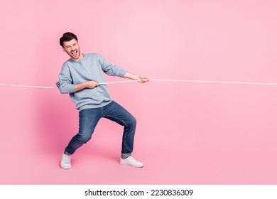Full length photo of excited guy playing tug war game pull string isolated on pastel color background