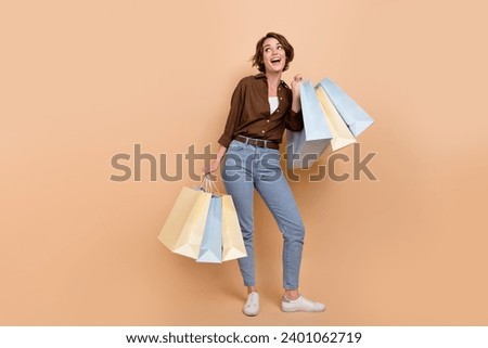 Full length photo of excited impressed lady wear brown shirt holding bargains looking empty space isolated beige color background