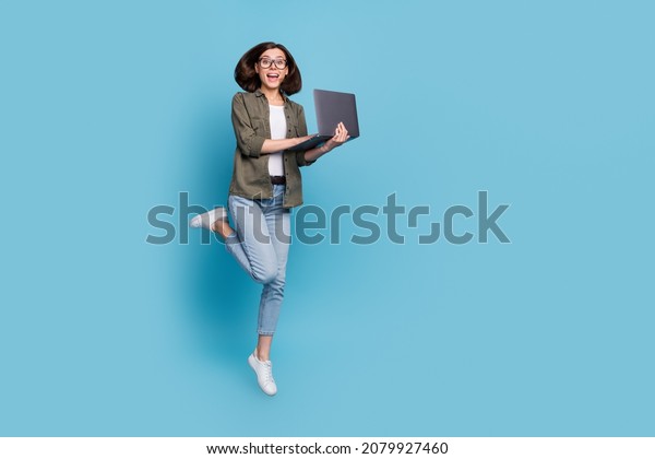 Full length photo of excited lady computer\
geek it developer jump use gadget wear shirt denim jeans isolated\
over blue color background