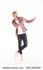 Full length photo of excited teen man 17y wearing plaid shirt exclaiming and pointing fingers aside on copyspace isolated over white background - Shutterstock ID 1051343339