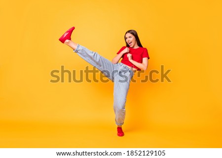 Full length photo focused girl practicing kicks raise leg exercise wear red crop top jeans isolated yellow color background