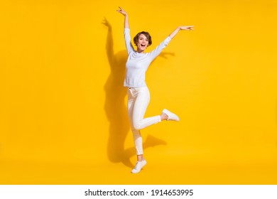 Full length photo of funky charming young lady dressed white shirt dancing rising hands arms isolated yellow color background
