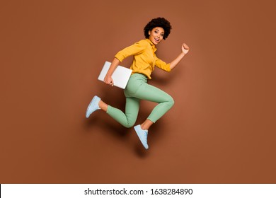 Full length photo of funky dark skin lady jump high hold notebook hurry classes lessons schoolgirl wear yellow shirt green pants footwear isolated brown color background