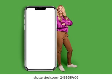 Full length photo of funky dreamy woman wear violet shirt arms crossed looking modern gadget empty space isolated green color background - Powered by Shutterstock