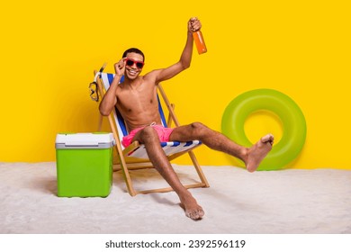 Full length photo of funky good mood shirtless man having fun lounge chair inviting drink beer isolated yellow color background - Powered by Shutterstock