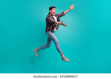 Full length photo of funky good mood man dressed plaid shirt jumping high catching arms empty space isolated turquoise color background