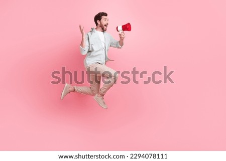 Full length photo of funky impressed man wear turquoise shirt shouting toa empty space jumping high isolated pink color background